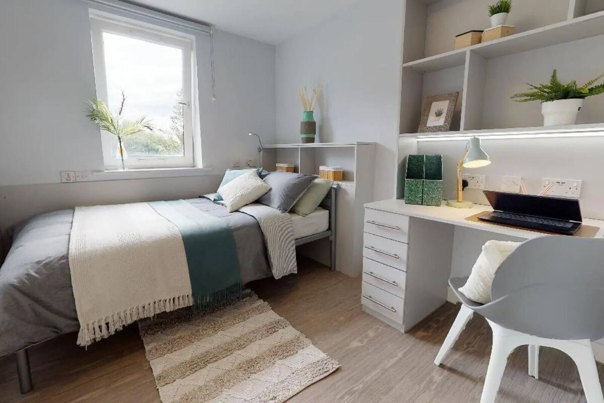Ein Schlafzimmer mit Bett, Schreibtisch, Stuhl und Regalen mit Pflanzen.