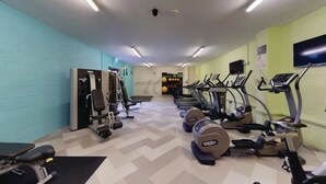 Ett gym med träningsutrustning, en väggmonterad TV och ett mönstrat golv.