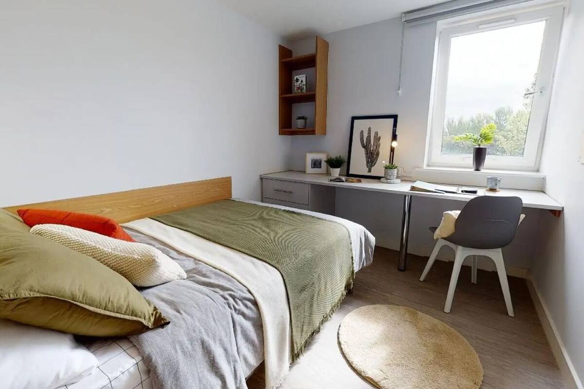 Ein Schlafzimmer mit Bett, Schreibtisch, Stuhl und einem Fenster mit Blick.
