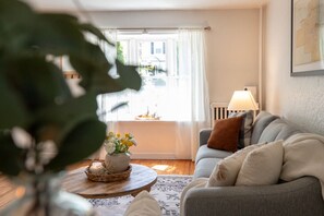 A cozy living room with a grey sofa, a round wooden coffee table, and a window with white curtains. - Charming Albany 1-BR Apt with beautiful patio to enjoy and off street parking (Albany)