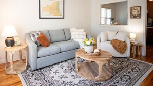 Un salon avec un canapé gris, un fauteuil blanc, une table basse en bois et un tapis à motifs.