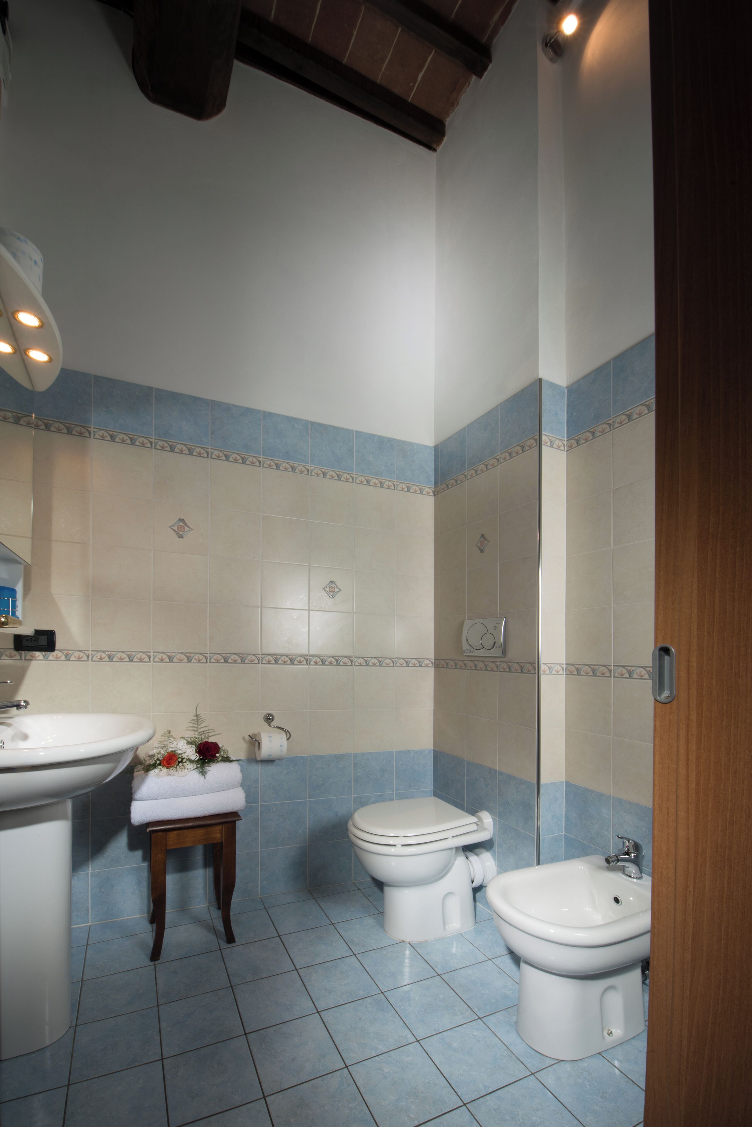 Ein Badezimmer mit Waschbecken, Toilette, Bidet und einem kleinen Hocker mit Handtuch.