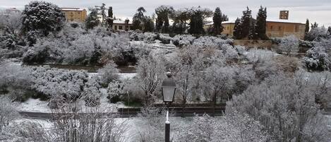 A snow-covered landscape with a street lamp, trees, and buildings in the background.