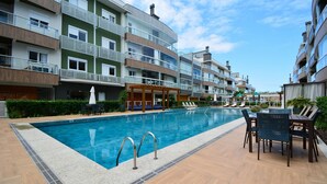 Une piscine dotée de chaises longues et d’un espace salon couvert, le tout entouré d’immeubles résidentiels à plusieurs étages.