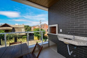 Een balkon met een houten tafel en stoelen, een spoelbak en uitzicht op naburige gebouwen.