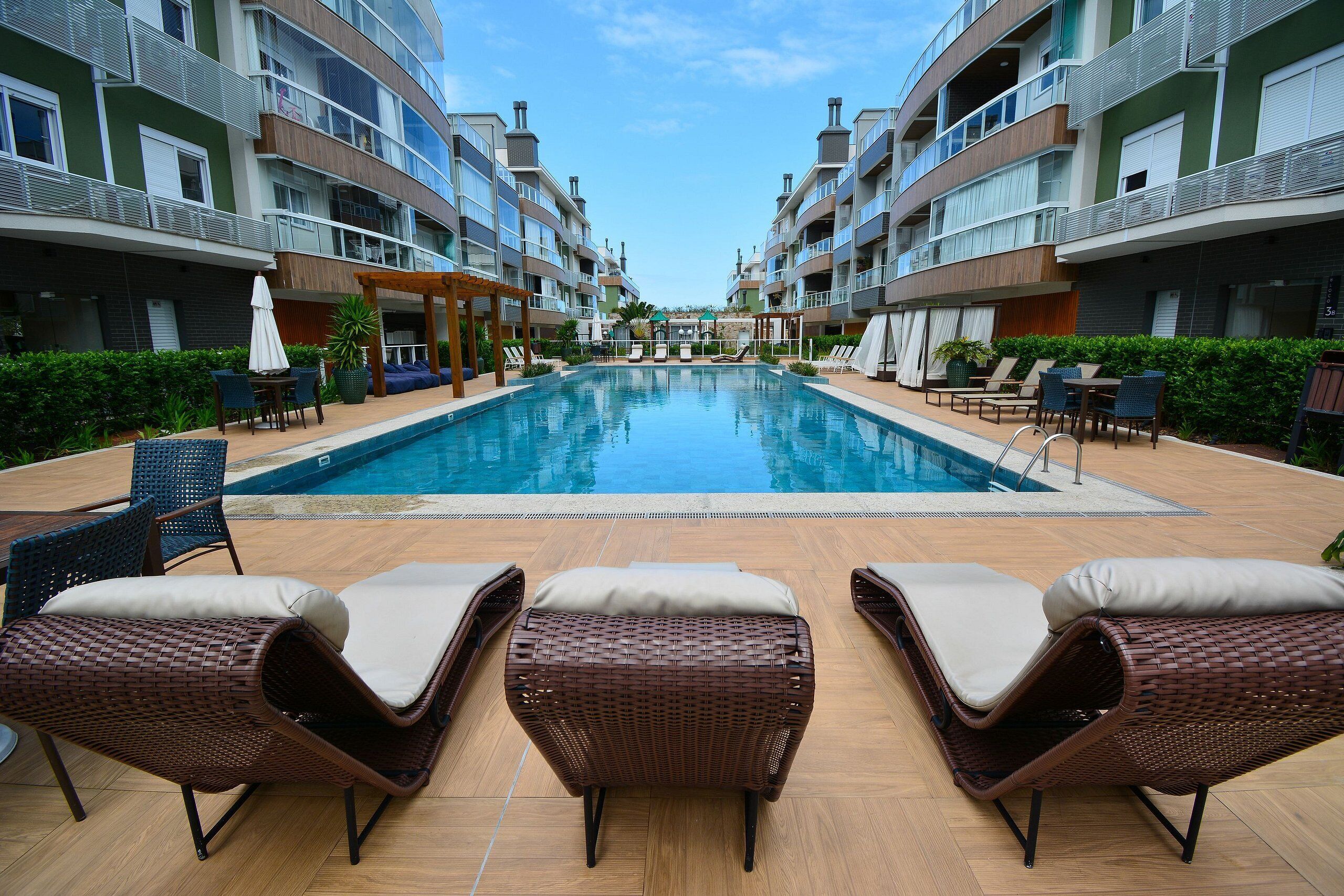 A swimming pool with lounge chairs and a pergola, surrounded by multi-story buildings with balconies.