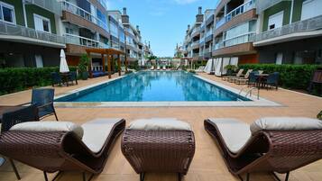 Una piscina con sillones de descanso y una pérgola, rodeada de edificios de varios pisos con balcones.
