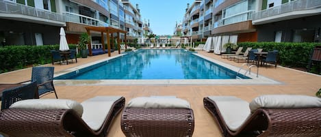 A swimming pool with lounge chairs and a pergola, surrounded by multi-story buildings with balconies.