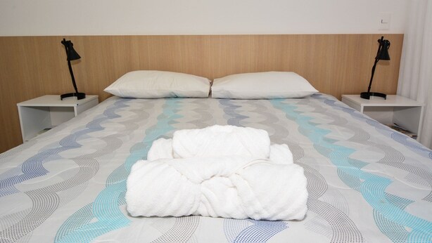 Un lit bien fait, recouvert d’une couvre-lit à motifs, avec deux oreillers blancs et deux tables de chevet dotées de lampes.
