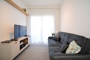 A living room with a flat-screen TV, a dark sofa, and a white entertainment unit. - SunClub-300 metros da Praia do Campeche (Florianopolis)