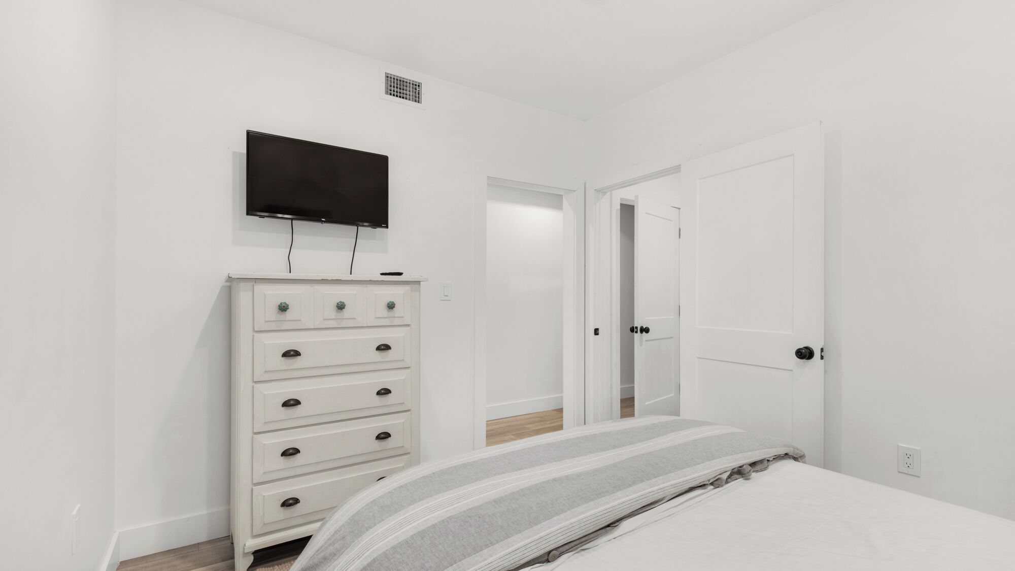 Quarto com cama, cômoda, televisão e porta que dá para outro espaço.