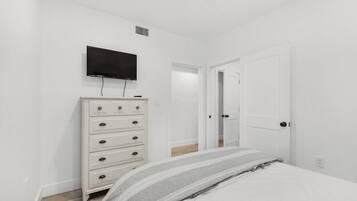 Quarto com cama, cômoda, televisão e porta que dá para outro espaço.