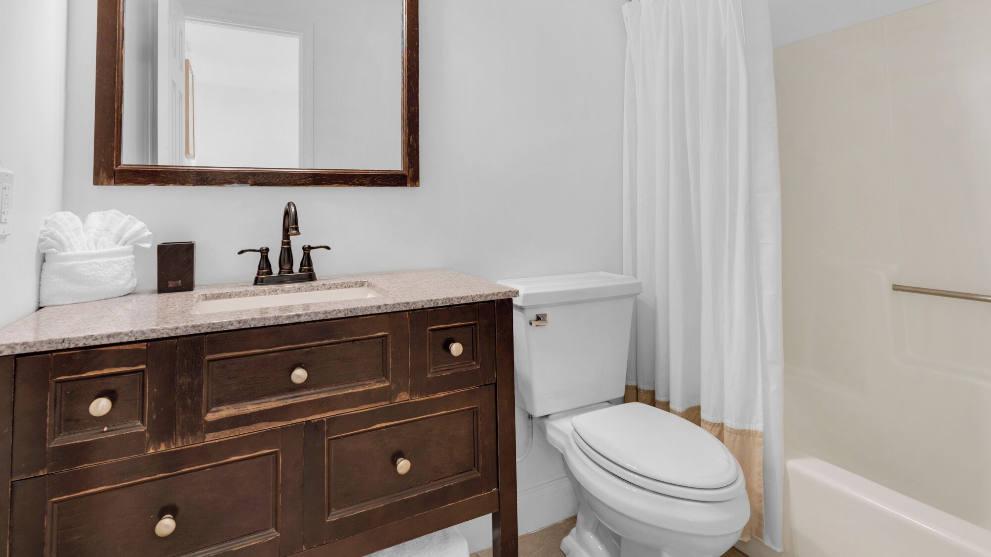 A bathroom with a wooden vanity, a white toilet, and a shower curtain.