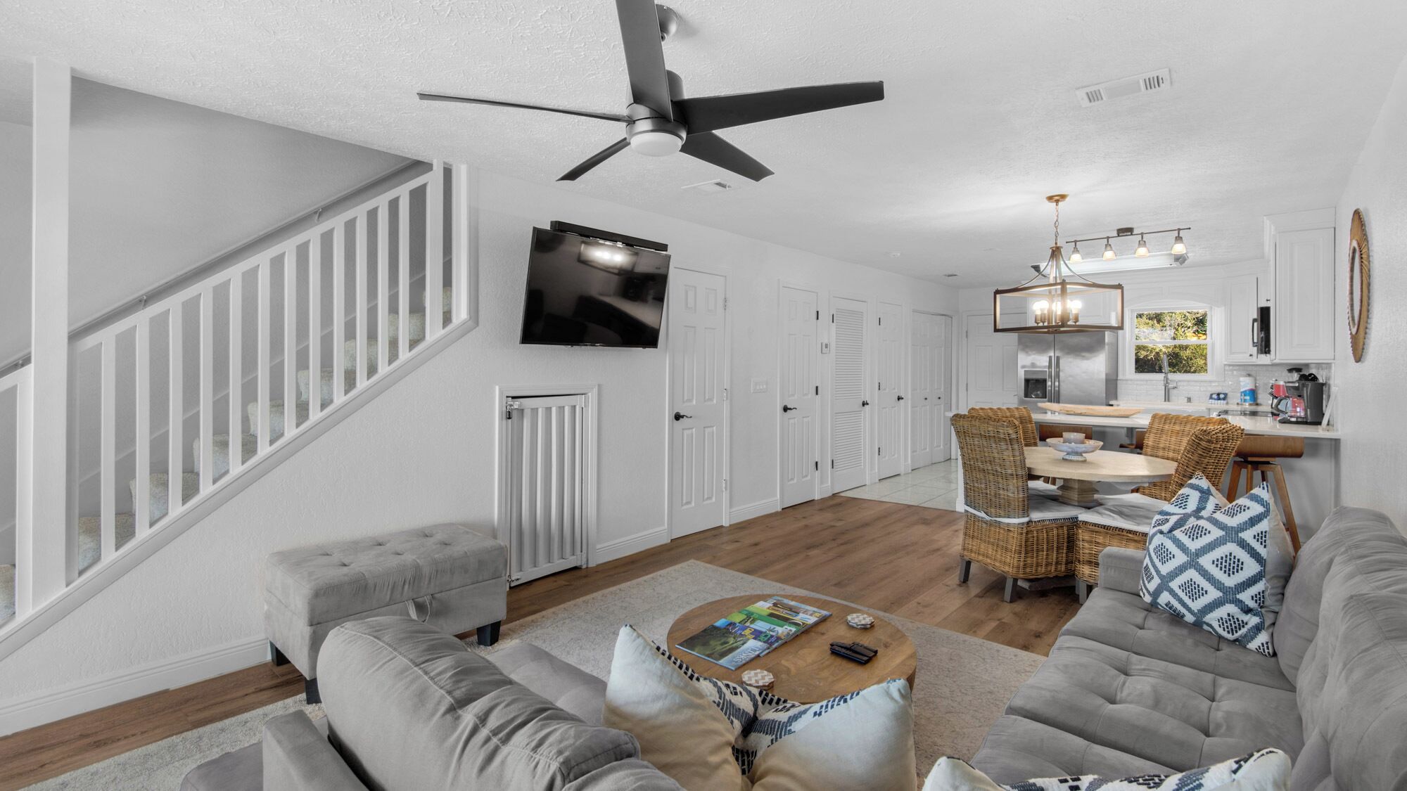 A modern living room with a grey sofa, a coffee table, and a dining area with wicker chairs.