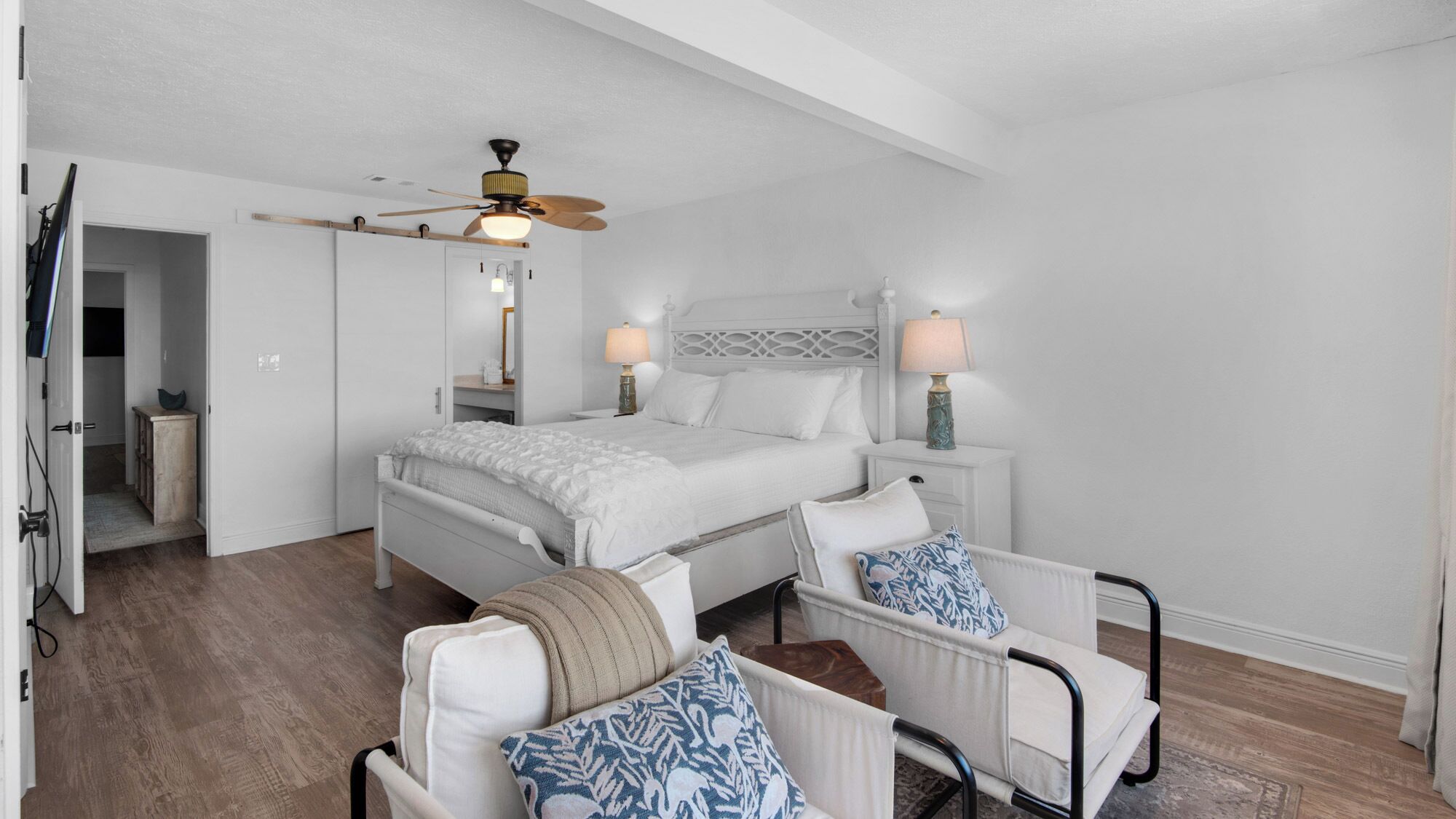 A bedroom with a bed, bedside tables, a chair, a ceiling fan, and a door.