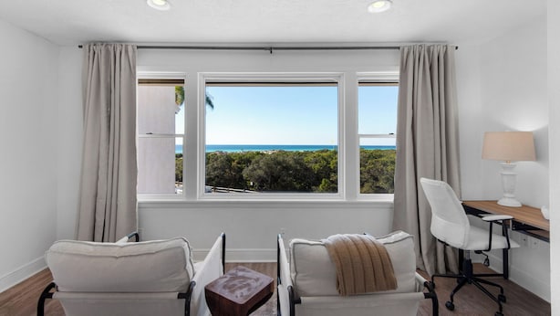 Una habitación con vista al océano, dos sillas, un escritorio con lámpara y una mesita.