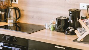 A kitchen with a modern stove, coffee maker, toaster, and various jars on the counter. - Le Sam PLay (Mussidan)