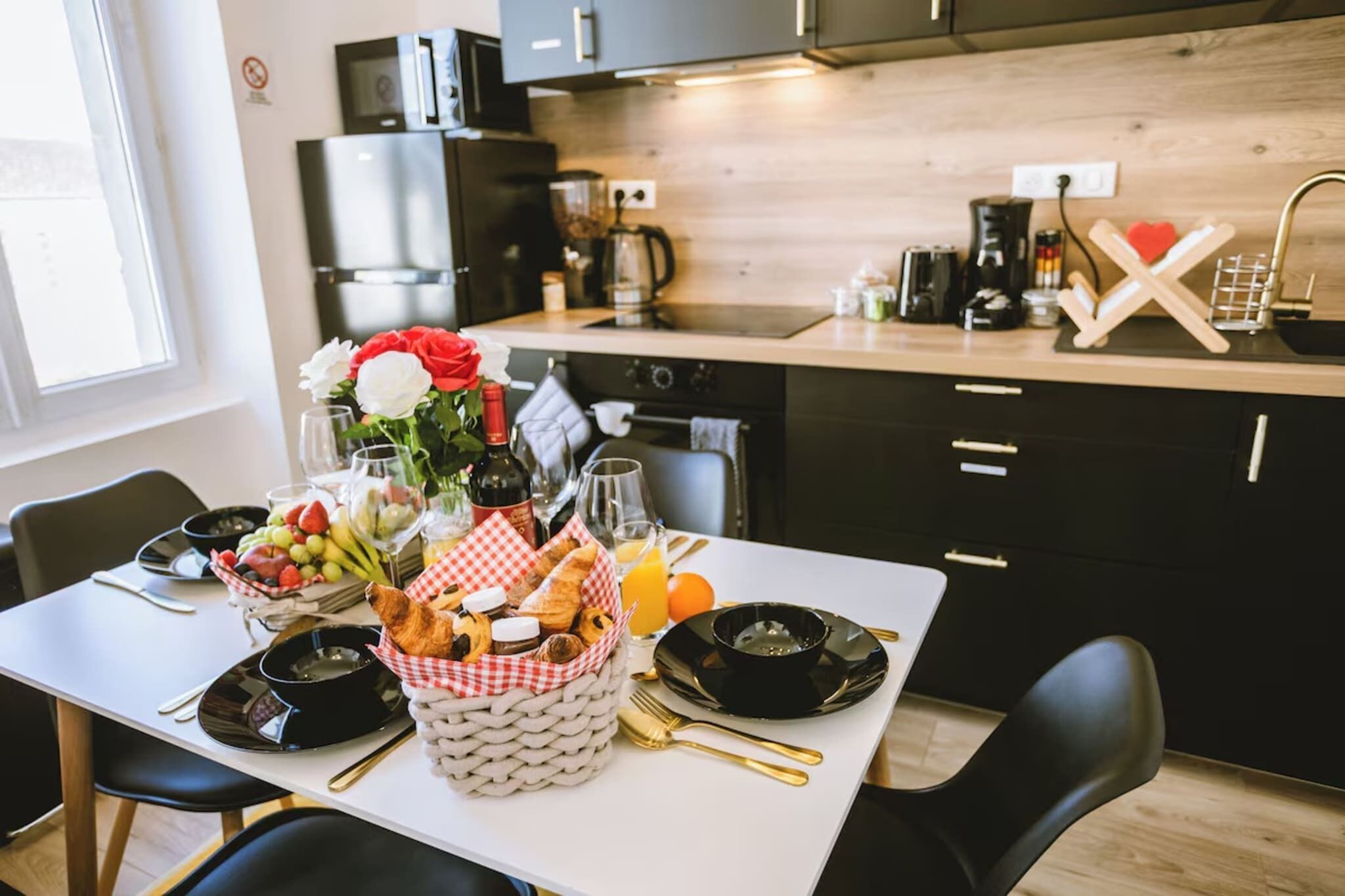 A breakfast setup with a table set for two, including plates, bowls, glasses, and a basket of bread and fruit.
