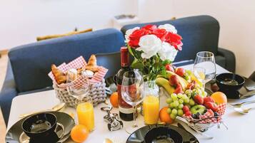 A breakfast table with croissants, a bottle of wine, a vase of flowers, and a fruit platter.