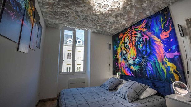 A bedroom with a bed, a window, a ceiling with a textured design, and a colorful tapestry on the wall. - Le Sam PLay (Mussidan)