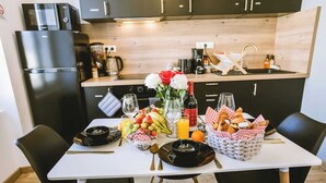 A modern kitchen with a dining table set for two, featuring a refrigerator, coffee maker, and a variety of fruits and pastries. - Le Sam PLay (Mussidan)
