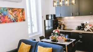 A modern kitchen with dark cabinets, a black refrigerator, and a dining area with a blue sofa and yellow cushions. - Le Sam PLay (Mussidan)