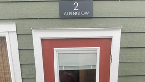 A red door with a white frame, a mailbox, and a sign above indicating the address as 2 Alpenglow. - Fresh Studio Apartment in Central Rossland (Rossland)