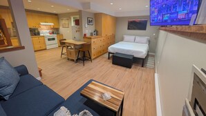 A compact living space with a kitchenette, a dining area, a bed, and a television. - Fresh Studio Apartment in Central Rossland (Rossland)