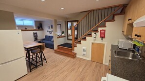 A compact kitchen with a wooden staircase, a dining area with a table and chairs, and a built-in microwave. - Fresh Studio Apartment in Central Rossland (Rossland)