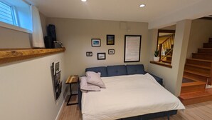 A bedroom with a large bed, a wooden headboard, a small bedside table, a wall-mounted shelf, and a staircase. - Fresh Studio Apartment in Central Rossland (Rossland)