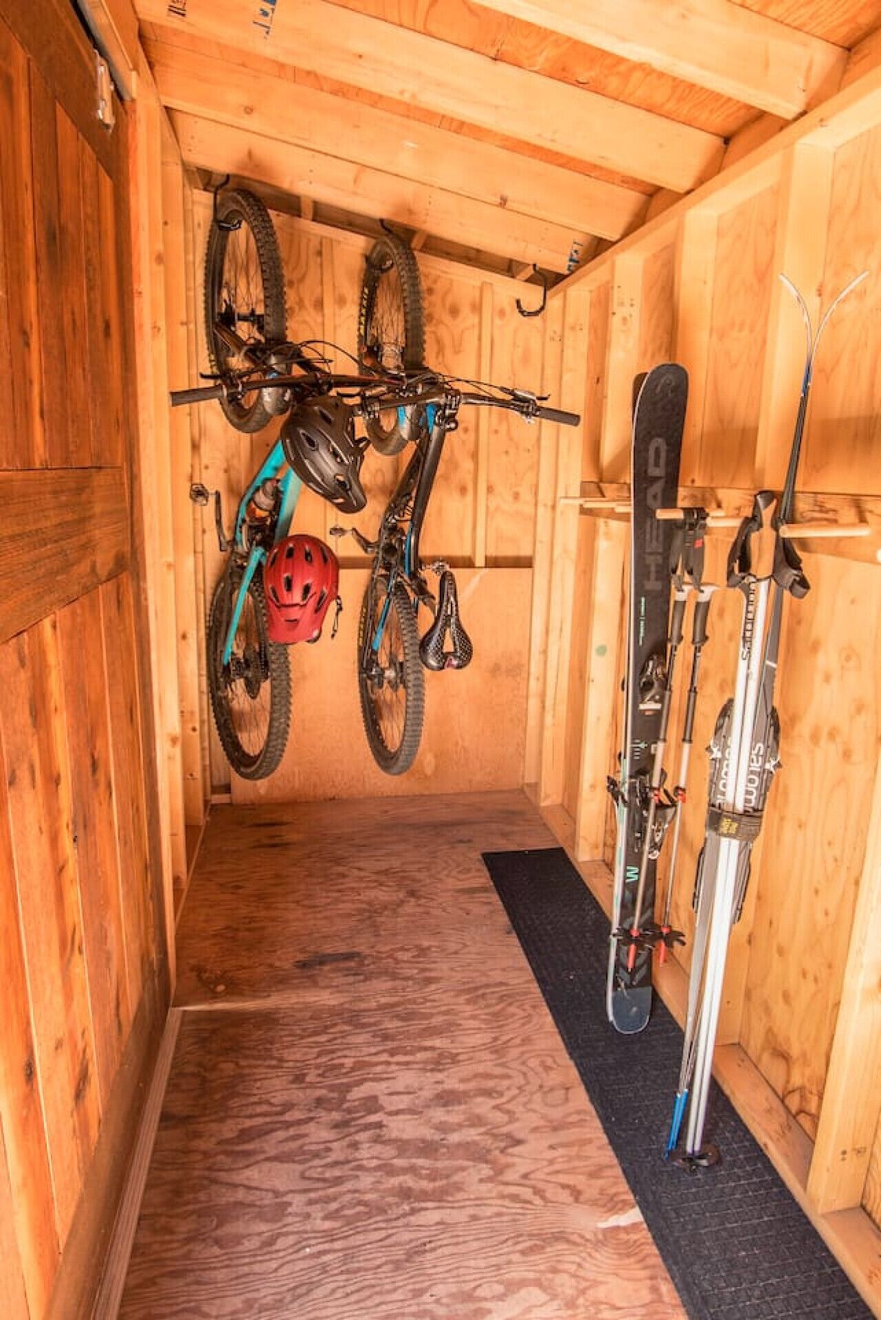 A wooden room with a bike and skis hanging on the wall.
