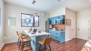 A modern kitchen with a central island, bar stools, and blue cabinets. - Sparkling NEW Rossland Midtown Studio Apartment (Rossland)