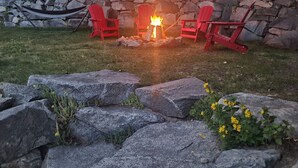 A stone fire pit with red Adirondack chairs around it. - Sparkling NEW Rossland Midtown Studio Apartment (Rossland)