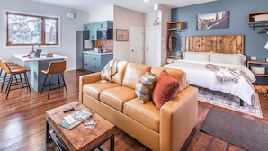 A modern apartment with a kitchen, a dining area, a living room with a sofa, and a bedroom with a bed. - Sparkling NEW Rossland Midtown Studio Apartment (Rossland)