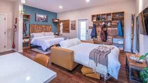 Ein Hotelzimmer mit zwei Betten, einem Schreibtisch, einem Stuhl, einem kleinen Tisch, einem Spiegel und einem Kleiderständer mit Jacken.