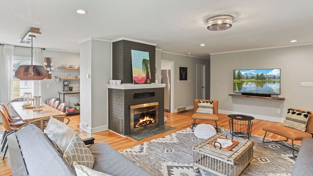A modern living room with a fireplace, comfortable seating, a dining area, and a TV mounted on the wall.