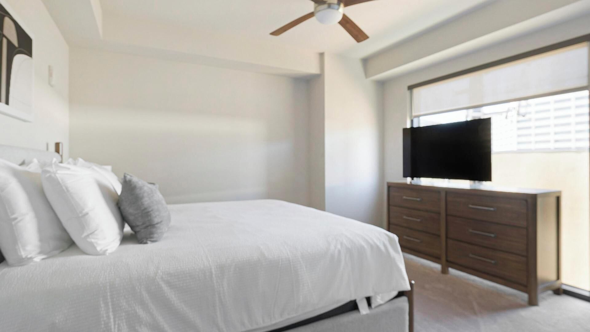 A bedroom with a bed, a ceiling fan, a dresser, and a TV.