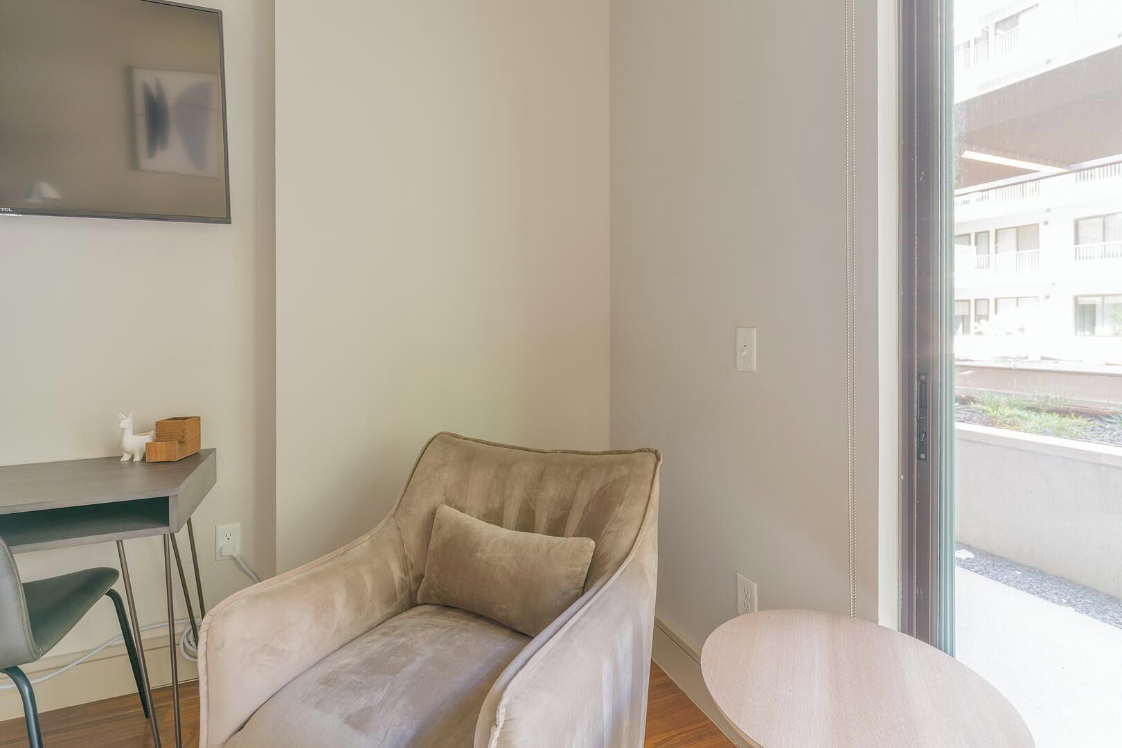 A modern room with a beige sofa, a small table, and a chair. There is a window with a view of buildings outside.