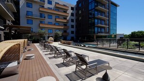 A rooftop pool area with lounge chairs, a wooden deck, and a modern building in the background. - Landing Apartments Houston (Houston)