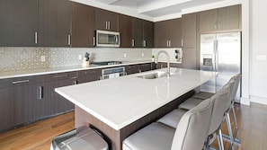 Una cocina moderna con armarios de madera oscura, una isla grande con taburetes de bar, electrodomésticos de acero inoxidable y un salpicadero geométrico.