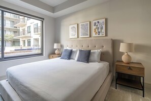 Habitación de hotel moderna con una cama grande, dos mesitas de noche y un ventanal con vistas al exterior del edificio.