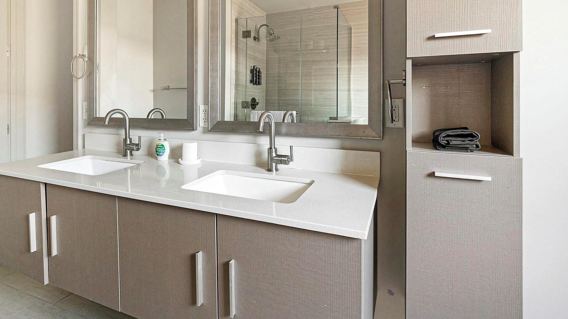 Une salle de bain moderne avec deux lavabos, un grand miroir et une cabine de douche.
