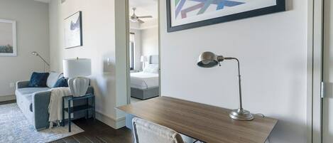 Habitación de hotel moderna con un escritorio de madera, una silla, una cama, un sofá y una mesita de noche con una lámpara.