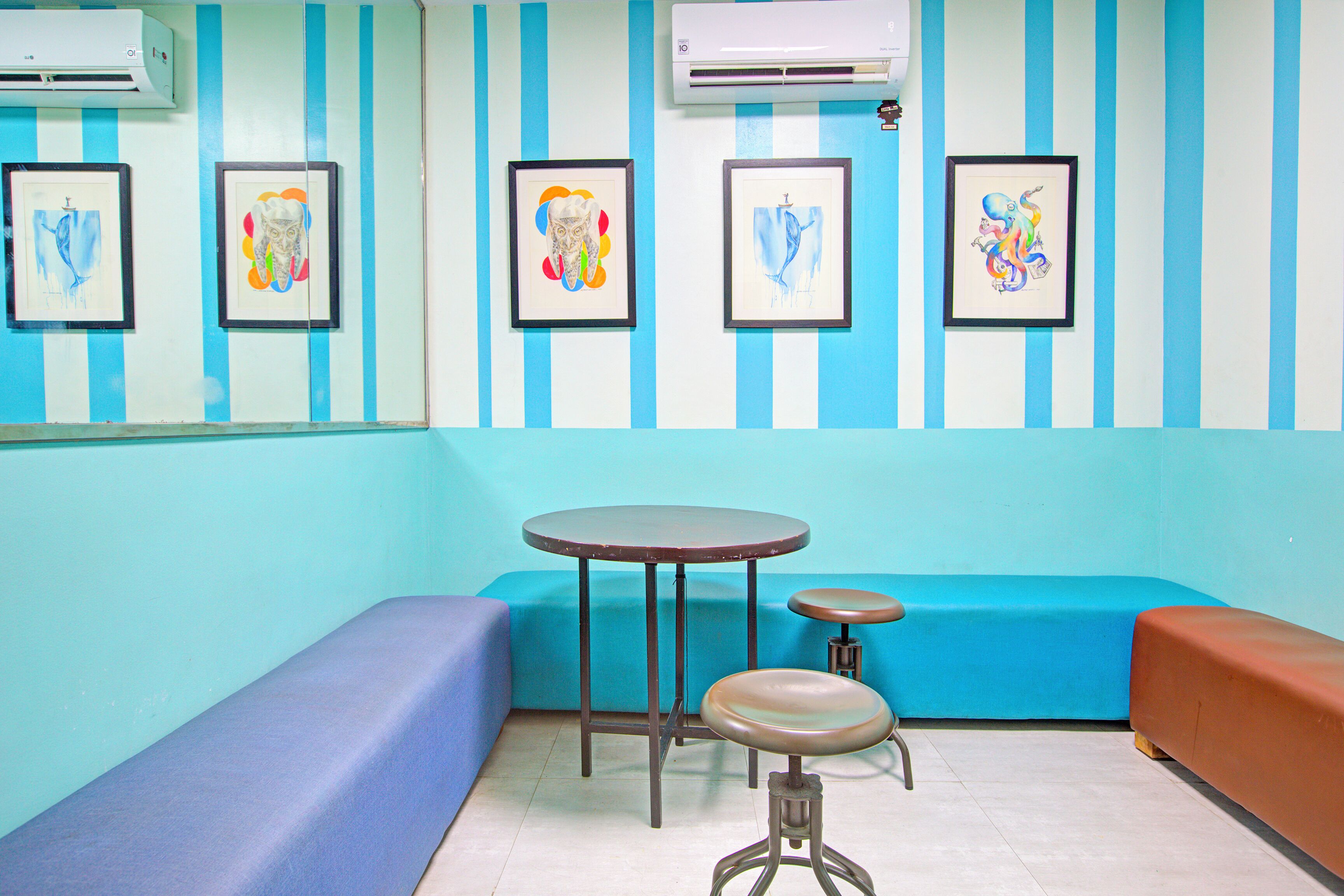 A room with a blue and white striped wall, a round table with a stool, a blue sofa, and a brown bench.