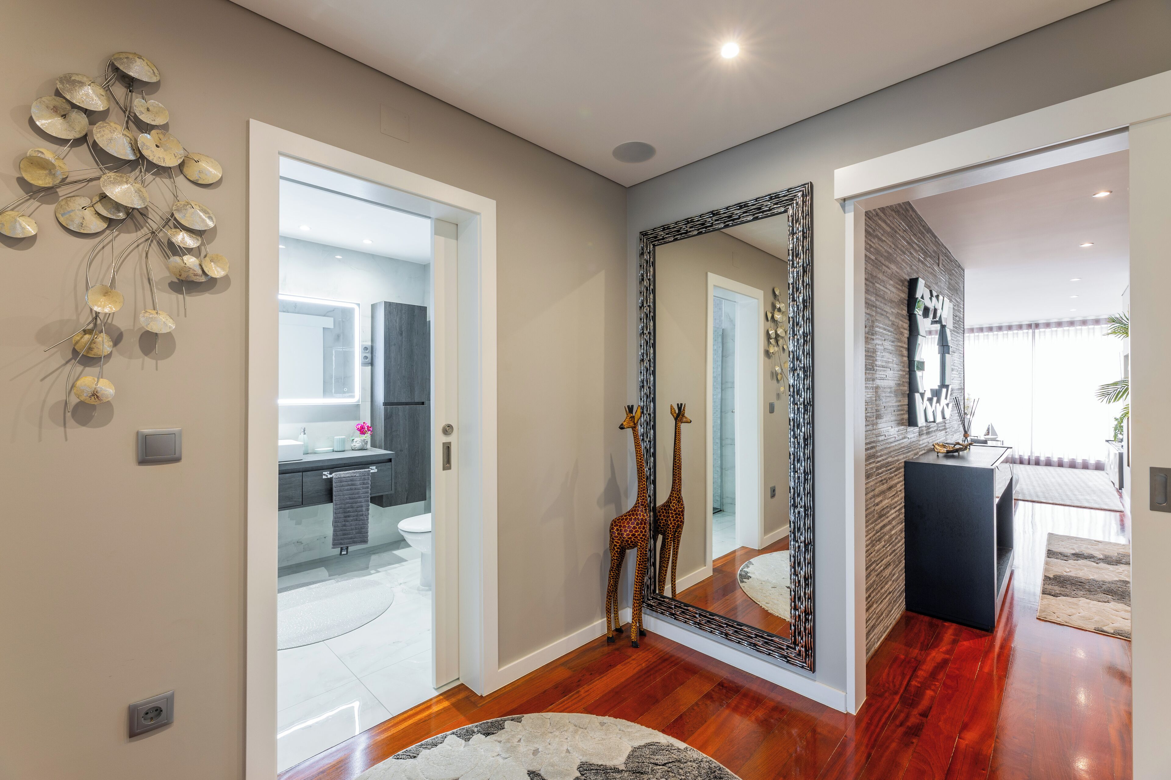 A modern interior with a wooden floor, a mirror, and a giraffe decoration.