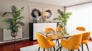 A dining area with a glass table, four yellow chairs, a black cabinet, and two potted plants. - Spacious and comfortable apartment in Apulia, 100 m from the beach! (Apúlia)