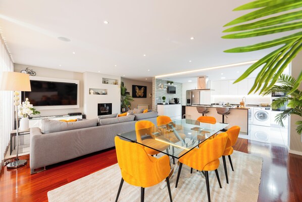 A modern living room with a glass dining table, sofa, and kitchen area. - Spacious and comfortable apartment in Apulia, just 100 meters from the beach! (Apúlia)