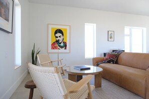 Ein Wohnzimmer mit einem braunen Ledersofa, einem runden Glastisch, einem weißen gewebten Sessel und einem gerahmten Gemälde an der Wand.
