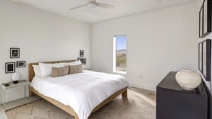 A bedroom with a bed, a nightstand, a dresser, a vase, and a window with a view.