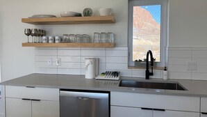 A modern kitchen with a dishwasher, a sink, and a window with a view of a desert landscape.